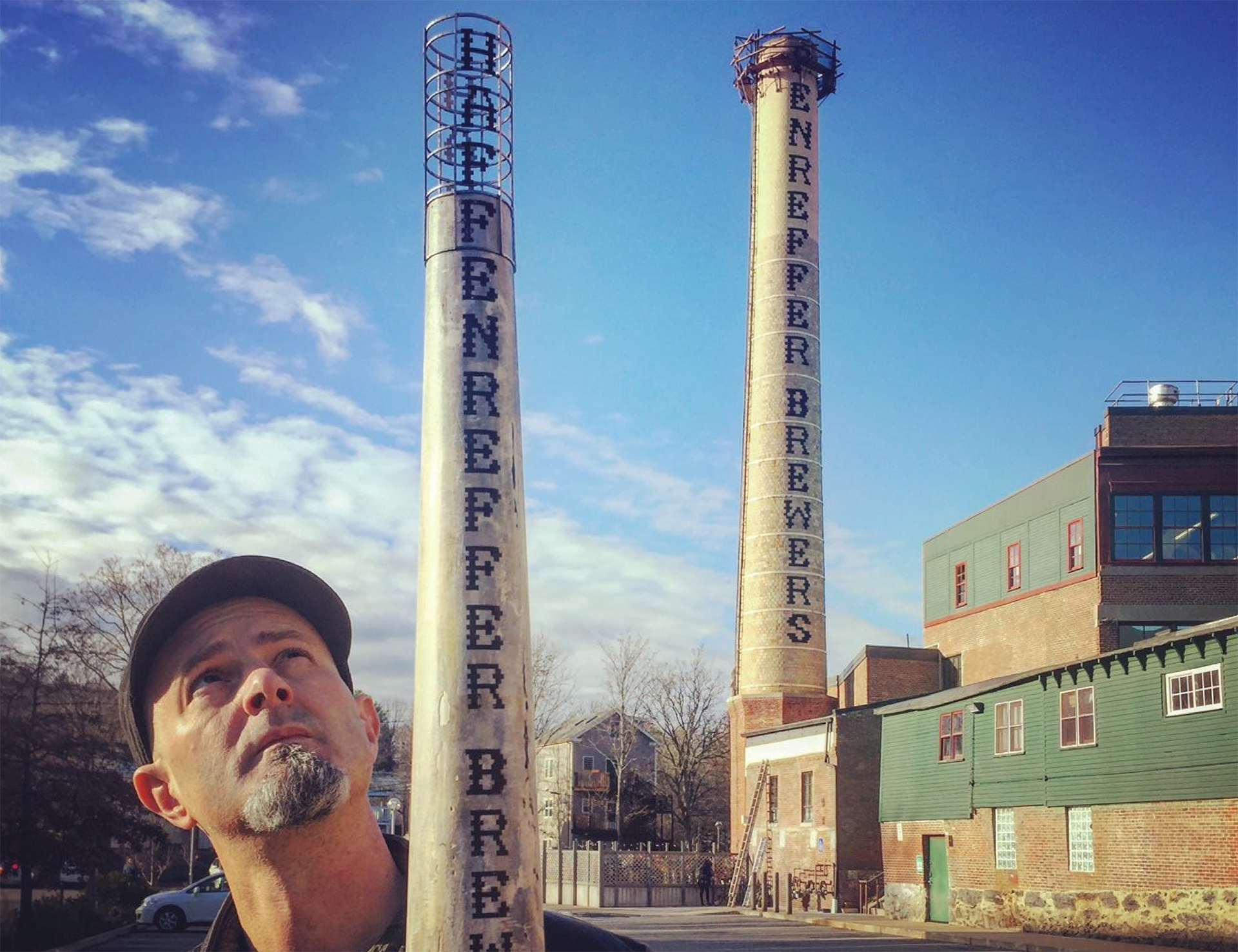Artist Robert Maloney with his model of the Haffenreffer Brewery Chimney Restoration standing in front of the in-process project.